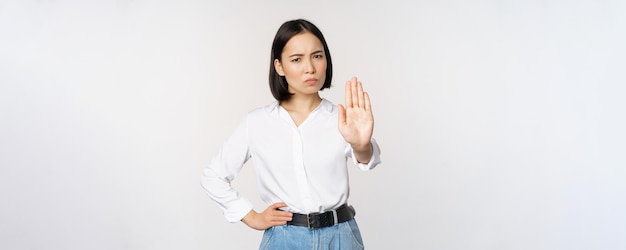 Portret van een jonge vrouw die één hand uitsteekt, stop taboe-teken dat iets afwijst dat op een witte achtergrond staat