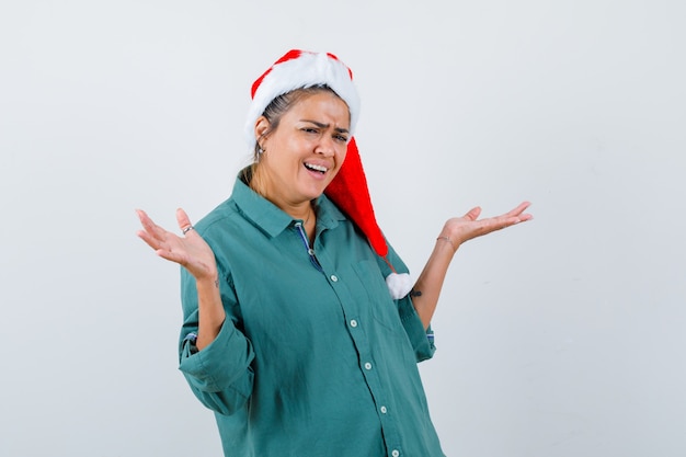 Portret van een jonge vrouw die een hulpeloos gebaar in een overhemd, een kerstmuts en een hulpeloos vooraanzicht toont