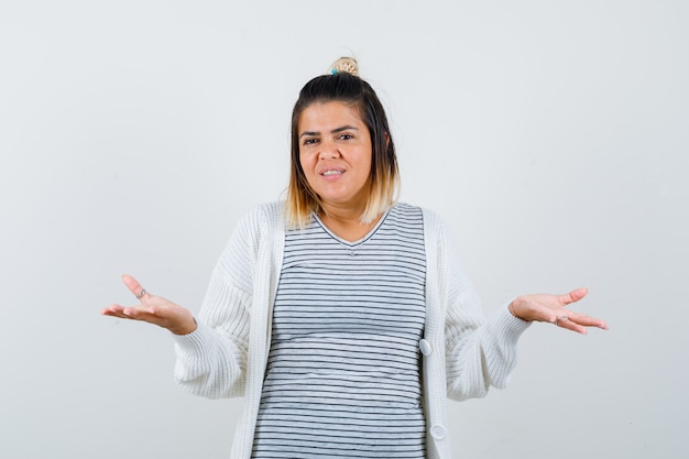 Portret van een jonge vrouw die een hulpeloos gebaar toont in een t-shirt, vest en een gelukzalig vooraanzicht