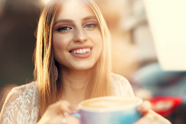 Portret van een jonge vrouw die een kop van koffie heeft en door het venster kijkt