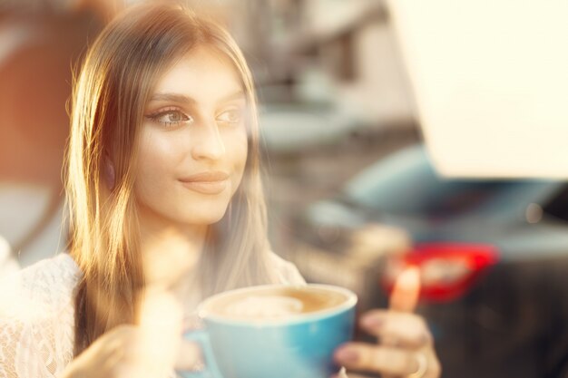 Portret van een jonge vrouw die een kop van koffie heeft en door het venster kijkt