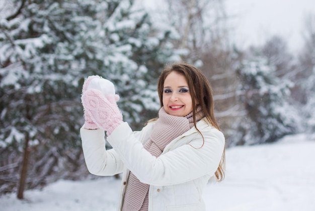 Portret van een jonge vrouw die een sneeuwbal gooit en naar de camera kijkt De vrouw gekleed in warme kleren staat in de winter buiten