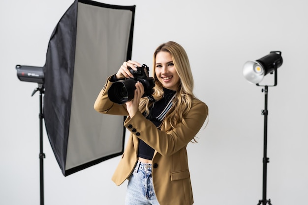 Portret van een jonge vrouw die foto's maakt met een professionele camera in de studio met verlichting op de achtergrond