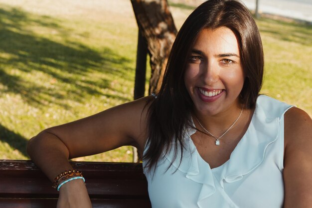 Foto portret van een jonge vrouw die glimlacht terwijl ze op een bankje in het park zit