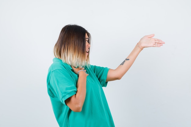 Portret van een jonge vrouw die handdruk aanbiedt, de hand op de borst houdt in een poloshirt en een verbijsterd vooraanzicht kijkt