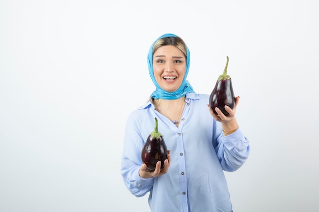 Portret van een jonge vrouw die in blauwe sjaal ongekookte aubergines houdt