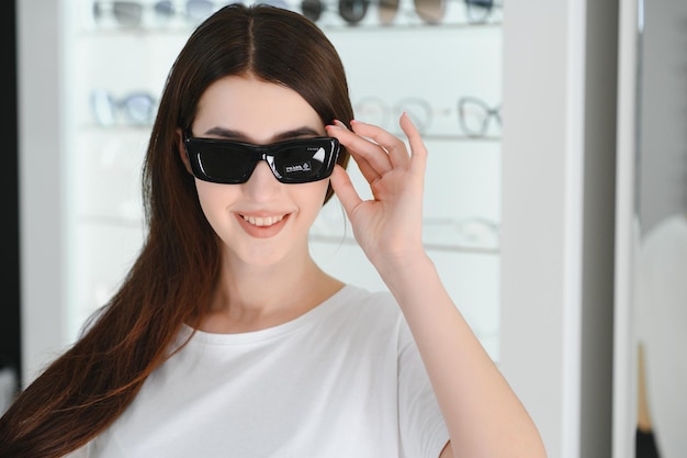 Portret van een jonge vrouw die in de winkel staat en een zonnebril probeert in de buurt van een spiegel