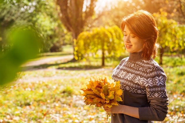 Portret van een jonge vrouw die in een de herfstpark glimlacht met bladeren in haar handen