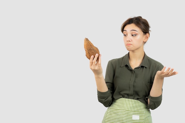 Portret van een jonge vrouw die in schort een kokosnoot houdt tegen witte muur