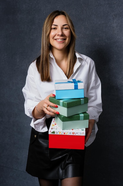 Portret van een jonge vrouw die met een glimlach in de camera kijkt en dozen met geschenken vasthoudt op een donkere achtergrond