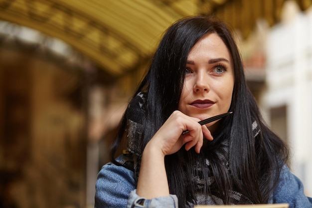 Portret van een jonge vrouw die met pen in café zit