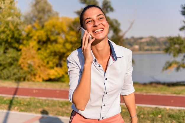 Portret van een jonge vrouw die mobiele telefoon gebruikt in het park bij de rivier