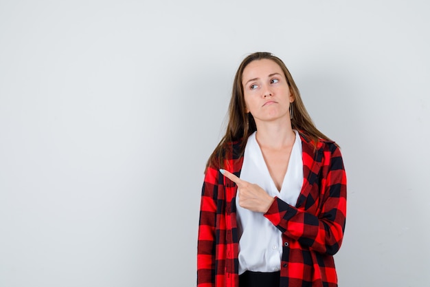 Portret van een jonge vrouw die naar de linkerbovenhoek wijst, wegkijkt in vrijetijdskleding en er ongezellig uitziet