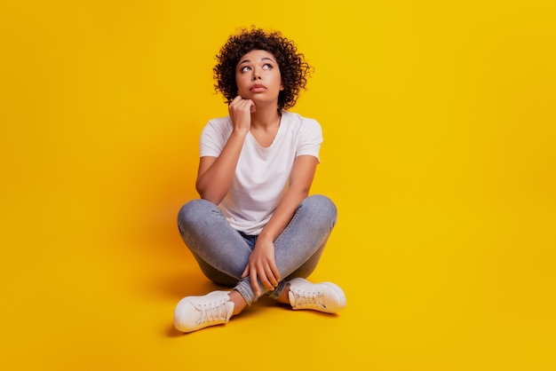 Portret van een jonge vrouw die nadenkt over iets dat op de vloer zit, op zoek naar gekruiste benen