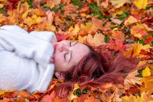 Portret van een jonge vrouw die op de grond ligt omringd door kleurrijke herfstbladeren