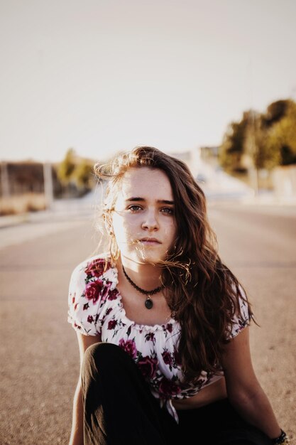 Foto portret van een jonge vrouw die op de weg tegen de lucht zit