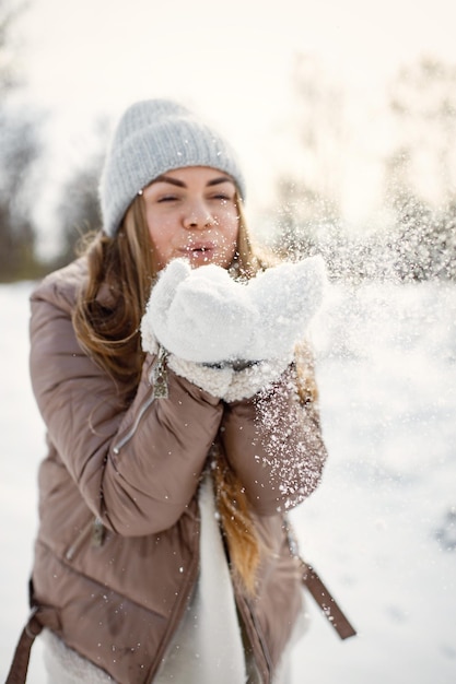 Portret van een jonge vrouw die op de winterdag in het bos staat en sneeuw blaast