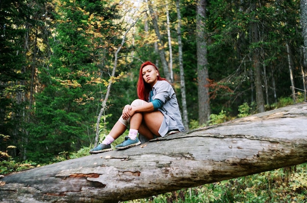 Portret van een jonge vrouw die op een boomstam in het bos zit
