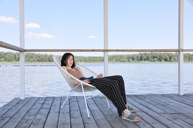 Foto portret van een jonge vrouw die op een pier zit boven de zee tegen de lucht