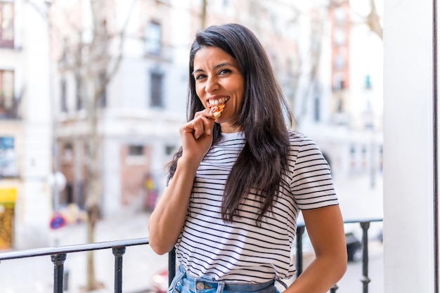 Portret van een jonge vrouw die pizza eet op een balkon in haar dagelijkse appartement thuis