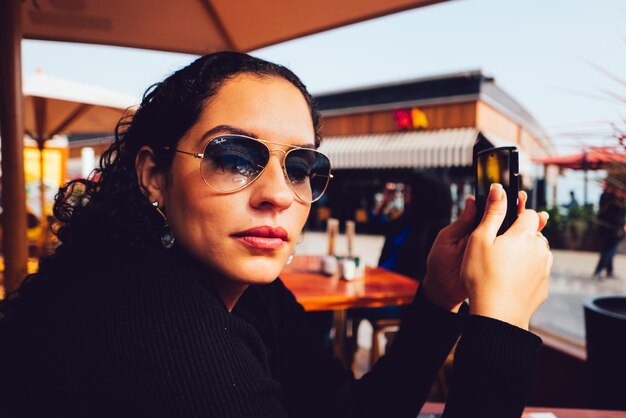 Portret van een jonge vrouw die sms't in een restaurant in de open lucht