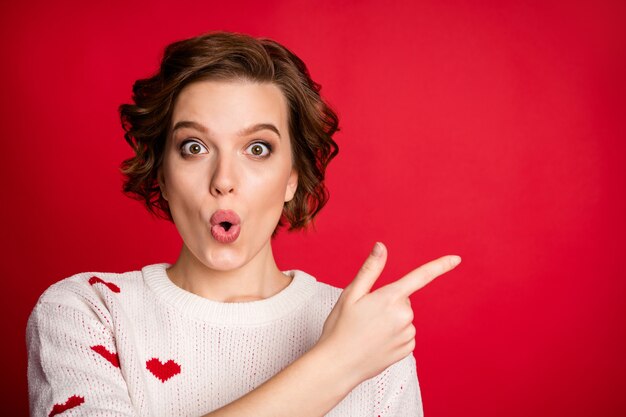 Portret van een jonge vrouw die stijlvolle trendy trui draagt geïsoleerd op rode muur