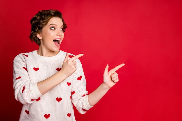 Portret van een jonge vrouw die stijlvolle trendy trui draagt geïsoleerd op rode muur