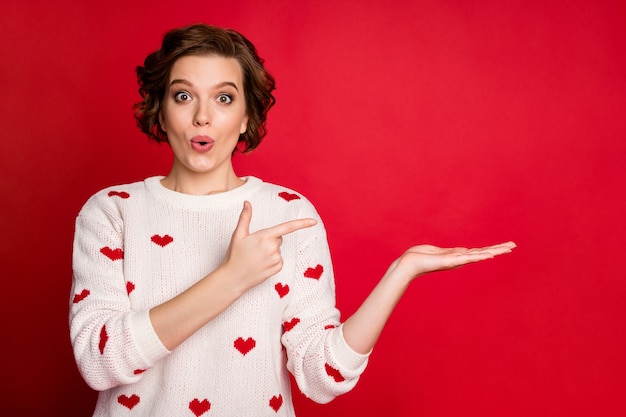 Portret van een jonge vrouw die stijlvolle trendy trui draagt geïsoleerd op rode muur