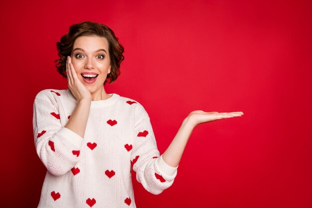 Portret van een jonge vrouw die stijlvolle trendy trui draagt geïsoleerd op rode muur