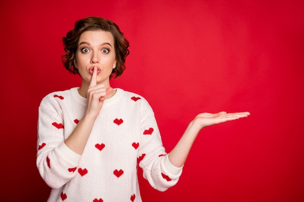 Portret van een jonge vrouw die stijlvolle trendy trui draagt geïsoleerd op rode muur