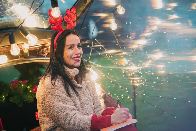 Portret van een jonge vrouw die tegen een verlichte kerstboom staat