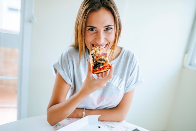 Portret van een jonge vrouw die thuis pizza eet