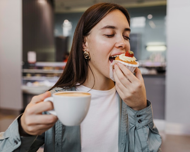 Portret van een jonge vrouw die van koffie en cake geniet