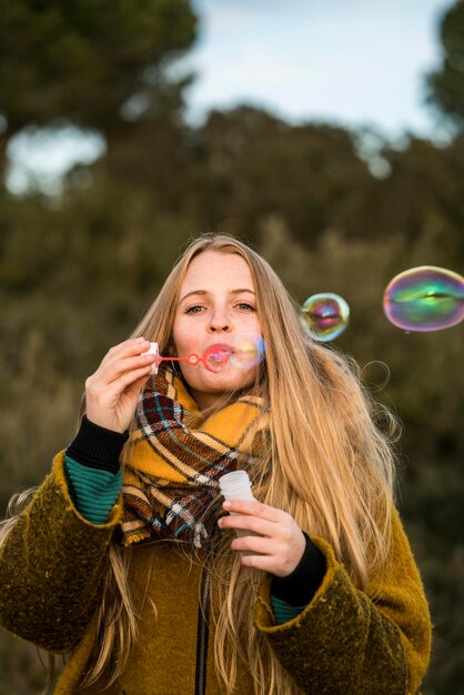 Foto portret van een jonge vrouw die zeepbellen blaast in de natuur