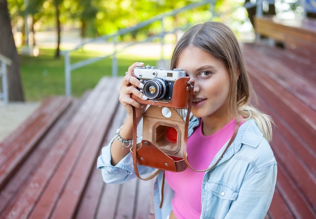 Foto portret van een jonge vrouw gekleed in stijlvolle kleding met een retro camera buitenshuis