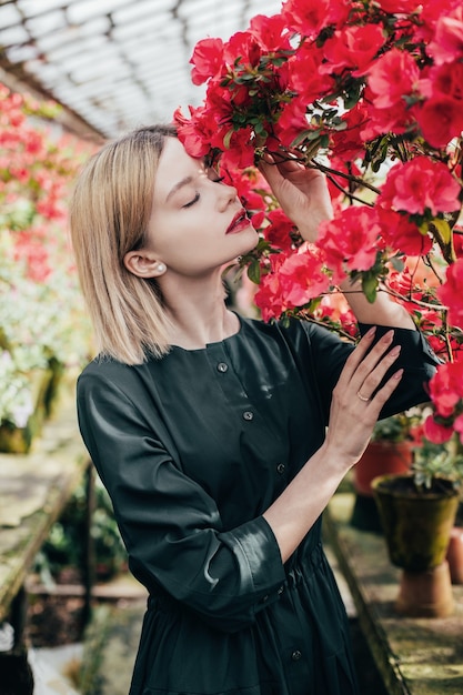 Portret van een jonge vrouw in een groene jurk in een kas met rode en roze bloeiende azalea's