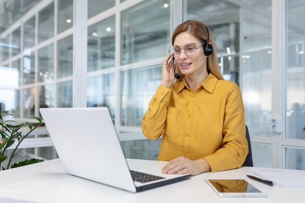 Portret van een jonge vrouw in een headset die online werkt in een kantoorcentrum vanaf een laptop