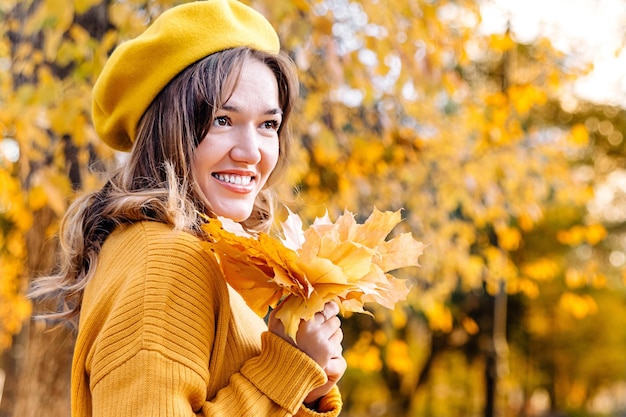 Foto portret van een jonge vrouw in een herfstpark een meisje in een gele baret lacht met esdoornbladeren sale