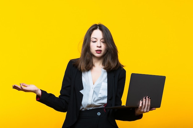 Portret van een jonge vrouw in een pak met een laptop op een gele achtergrond