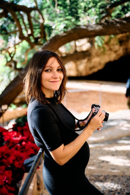 Foto portret van een jonge vrouw in een strakke jurk in de eerste maanden van haar zwangerschap die foto's maakt met een antieke camera