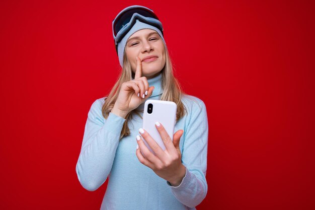 Portret van een jonge vrouw in een trui en skibril met een telefoon