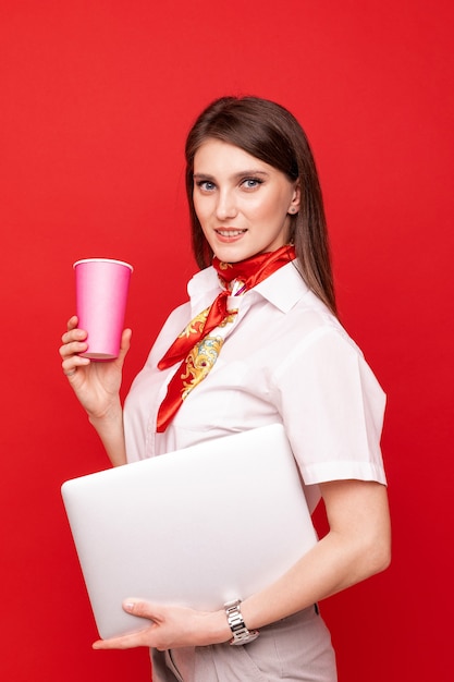 Portret van een jonge vrouw in een wit overhemd met laptop en een kop koffie