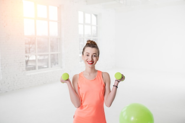 Portret van een jonge vrouw in sportkleding met halters en fitnessbal in de witte sportschool