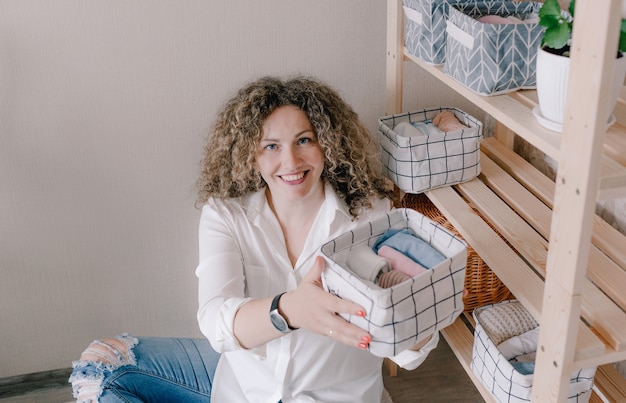 Portret van een jonge vrouw in vrijetijdskleding die prachtig dingen in containers en dozen stopt. Het concept van een goede opslag van accessoires en ondergoed in de kast