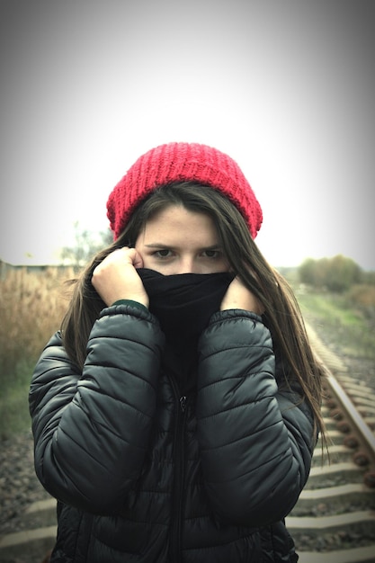 Foto portret van een jonge vrouw in warme kleding die in de winter tegen de lucht staat