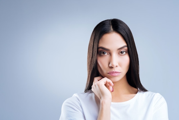 Portret van een jonge vrouw in wit t-shirt poseren tegen een grijze muur