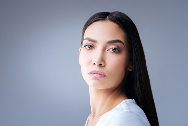 portret van een jonge vrouw in wit t-shirt poseren tegen een grijze muur