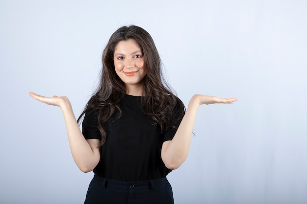 Portret van een jonge vrouw in zwarte outfit op zoek op een witte muur.