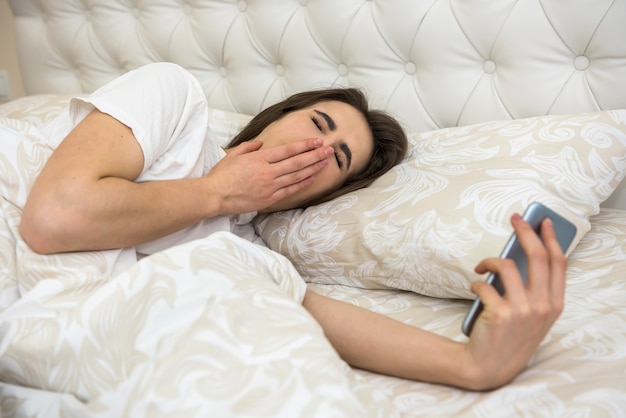 Portret van een jonge vrouw lag in de ochtend op het bed met telefoon in modern appartement. Wakker worden of slaapproblemen