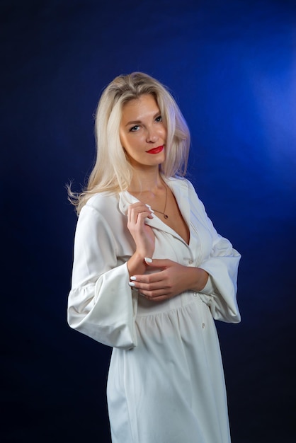 Portret van een jonge vrouw met blond haar in een witte jurk op een blauwe achtergrond in de studio